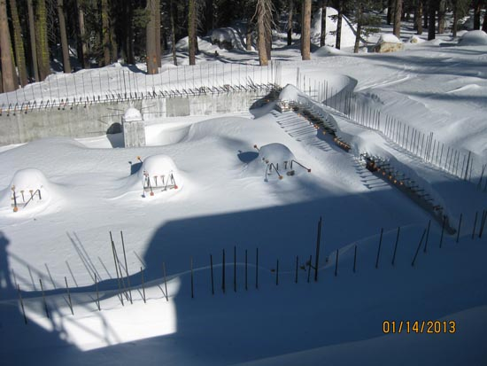 Snow-covered construction site with rebar protruding and forest background.