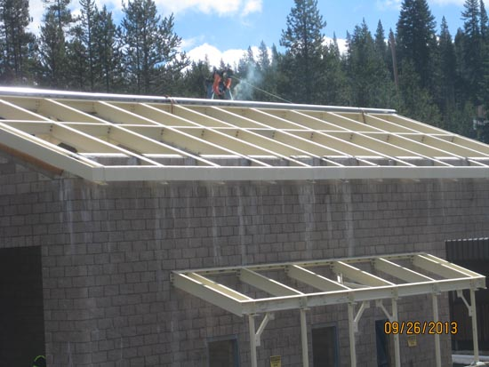 Building with partial roof, construction workers on top, trees in background.