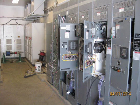 A room with open electrical panels and wiring, with various equipment and tools on the floor.