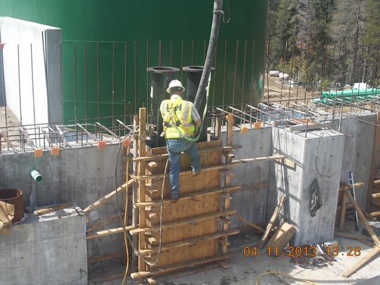 Construction worker with safety gear, pouring concrete into a formwork using a pump.