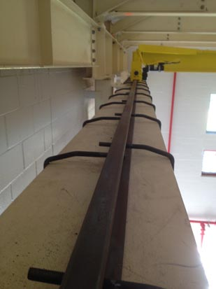 A vertical ladder attached to a wall inside an industrial building with overhead beams and windows.