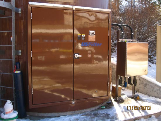 A brown metal tank with a USFilter logo and electrical panel, snowy ground.