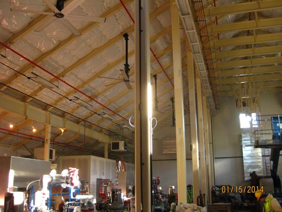 Large indoor industrial space with high ceiling, exposed beams, pipes, machinery, and construction activity.