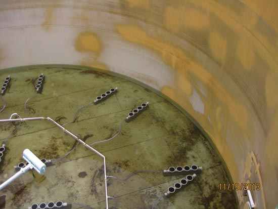 Interior of a large tank with pipes and fixtures on the floor. Patchy yellow areas on the walls.