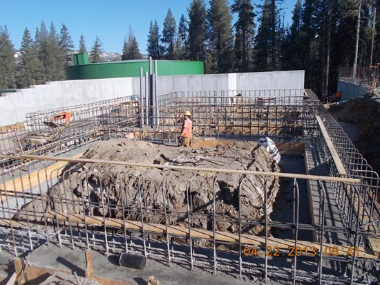 A construction site with metal framework, dirt, and a worker. Trees and structures are in the background. Date stamp: 04-22-2013.