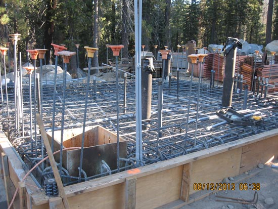 Construction site with reinforced steel rebar grid in a wooden frame, likely for a concrete foundation.