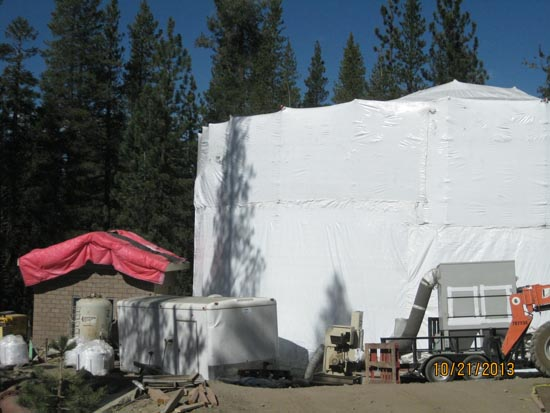 A large white covered building, red tarp on a smaller structure, containers, equipment, and trees in the background.