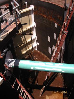 A large industrial tank interior with a green pipe and rust patches. Ladders provide access. Date on image: 05/28/2014.