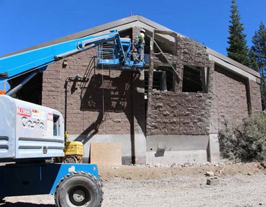 A construction worker in a lift is repairing or renovating a building exterior against a clear blue sky.