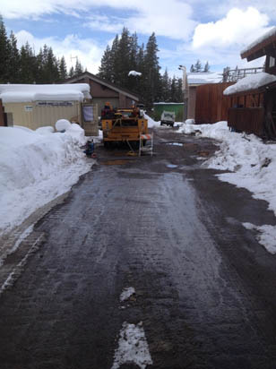 A snowy path with a vehicle, surrounded by buildings and trees under a cloudy sky.