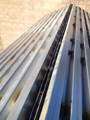 Corrugated metal sheets with rust spots, placed outdoors against a brick wall.