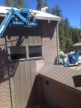 Workers using cherry pickers for maintenance on a brick building.