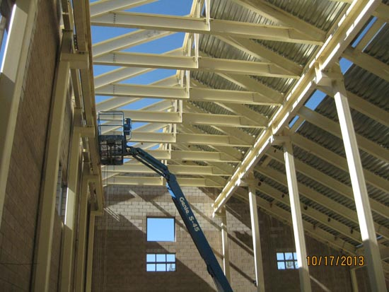A construction site with a blue lift inside a building, featuring steel beams and windows under a partially completed roof.