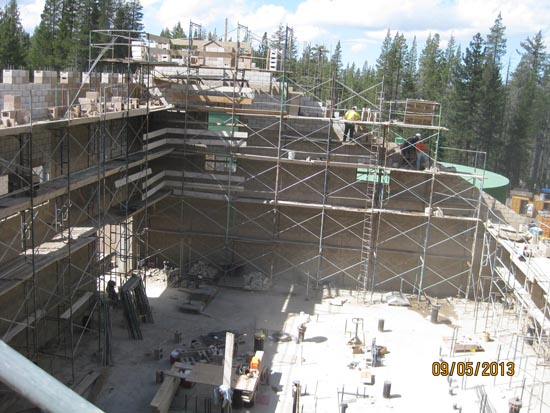 A construction site with scaffolding, workers, and building materials in a forested area.