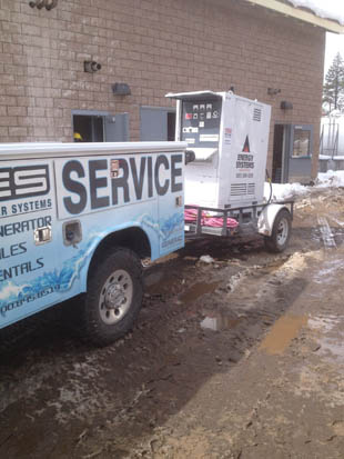 Service truck with attached equipment parked on a muddy street beside a building.