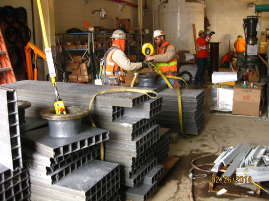 Construction workers wearing safety gear, organizing metal beams in a workshop.