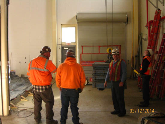 Four construction workers wearing safety gear in a building site with equipment and ladders.