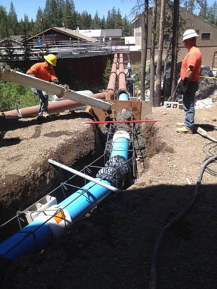 Workers installing a blue pipeline in a trench at a construction site.
