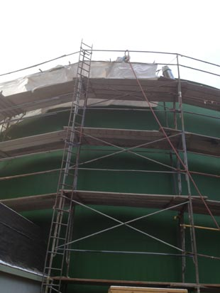 A green structure with scaffolding around it, covered at the top, likely under construction or maintenance.