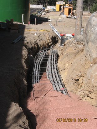 Construction site with rebar in a trench, surrounded by dirt and trees.