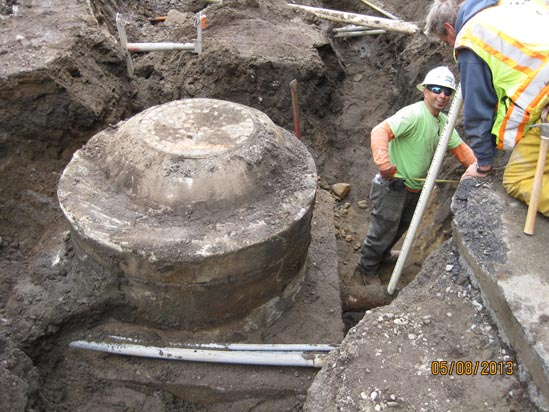 Construction workers inspecting a large, partially buried concrete structure at a dig site.
