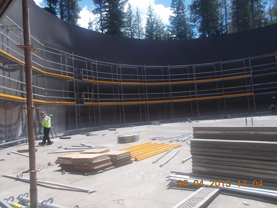 Construction site with scaffolding inside a large circular structure, materials on the ground, and a worker in a hard hat.