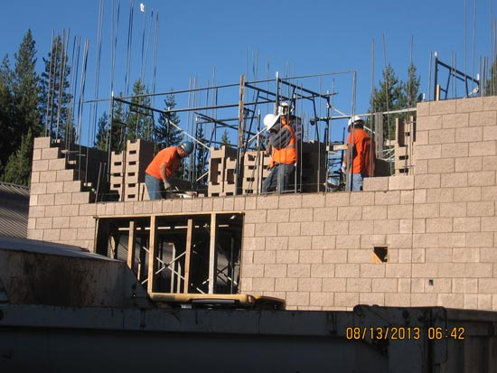 Construction workers in orange vests and helmets building a brick structure.