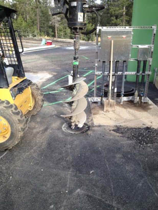 A construction auger attached to machinery, surrounded by tools and cable spools on a paved surface.