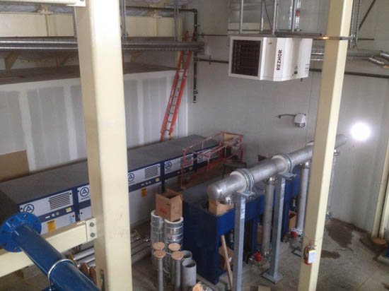 Industrial room with machinery, pipes, a ladder, and various equipment.
