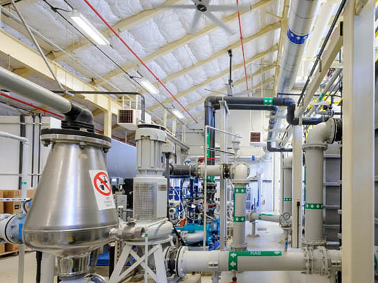 Industrial setting with metal pipes, ducts, and machinery inside a facility.