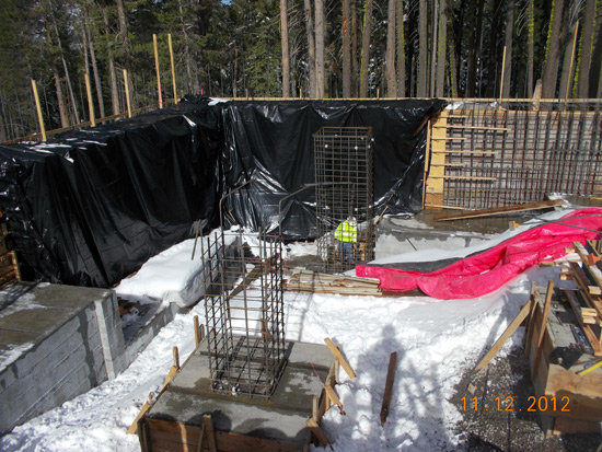Construction site with wooden frames, metal reinforcements, and tarps, surrounded by snow.