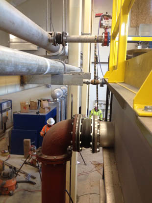 Industrial scene with large pipes, valves, and workers in safety gear inside a facility.