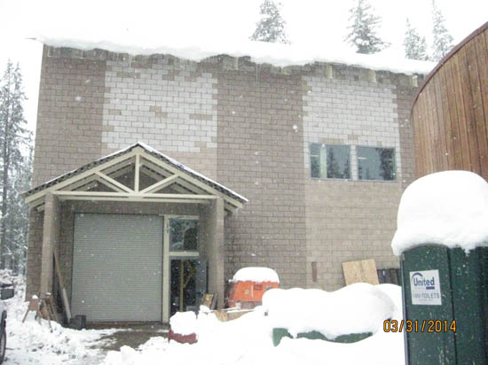 A snowy scene with a building under construction, featuring a garage door and a portable toilet.
