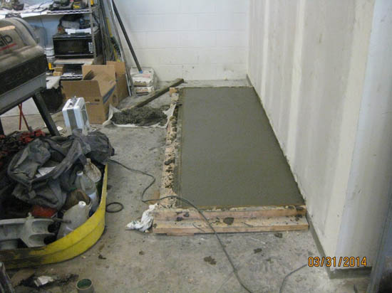 Concrete slab freshly poured inside a cluttered garage or workshop.