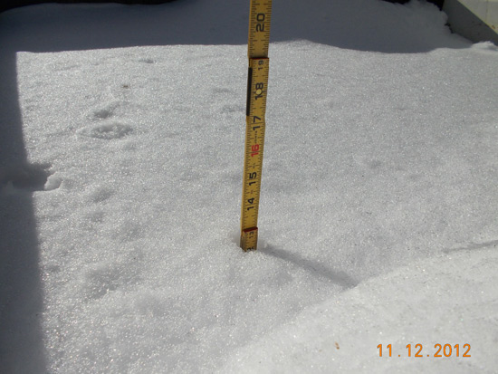 A measuring tape is standing in snow, showing a depth of around 15 inches.