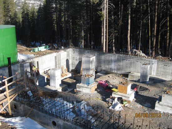 Construction site with concrete foundations and columns, surrounded by trees.