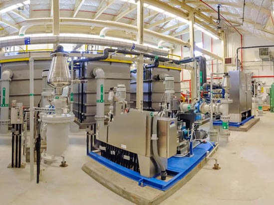 Industrial equipment and machinery inside a spacious factory or processing facility with overhead pipes and metal structures.