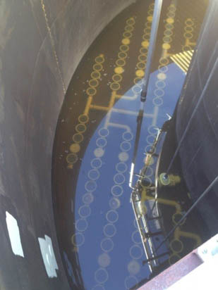The image shows a circular tank with water and submerged structures visible through the surface, likely part of an industrial facility.