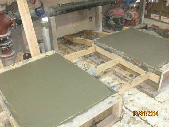 Two freshly poured concrete slabs in wooden frames, curing in a workshop environment.