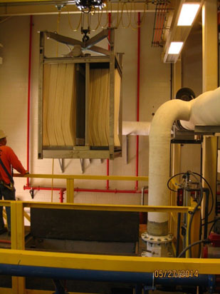 Industrial setup with a large machine holding stacked sheets, pipes, and a worker in a hard hat.