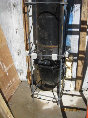 A vertical pipe encased in a rebar frame against a concrete and wooden background. Date stamp: 04/10/2013.