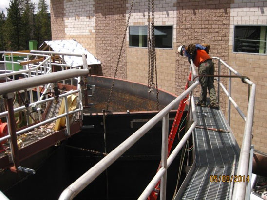 A worker in safety gear is on a platform inspecting a large industrial tank or structure.