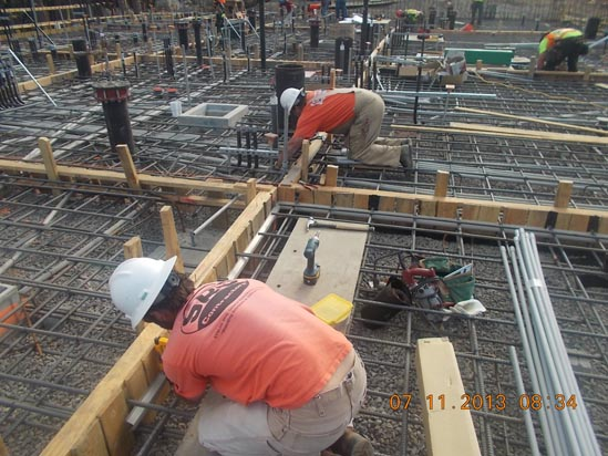 Construction workers are installing rebar and conduits on a building site.