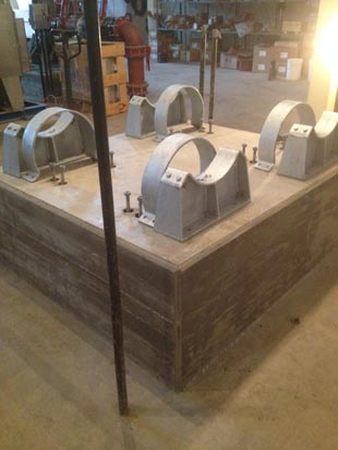 Four metal pipe supports mounted on a concrete pedestal in an industrial setting.