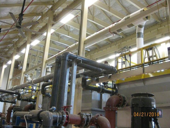 Industrial pipes and machinery inside a facility with a high ceiling and exposed beams.