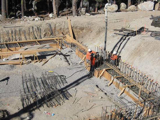 Construction site with workers pouring concrete into a form with metal reinforcements and surrounding materials.