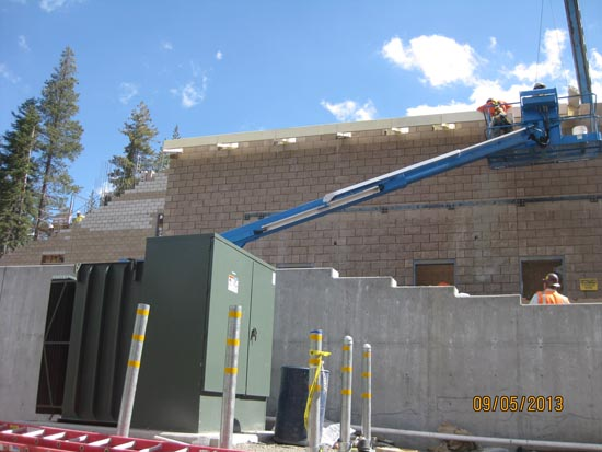 A construction site with workers, a lift platform, and a green utility box, set against a forested background.