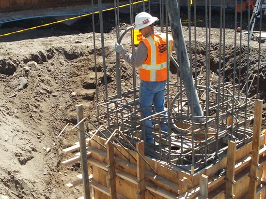 A construction worker in a hard hat and orange vest works with rebar on a building site.