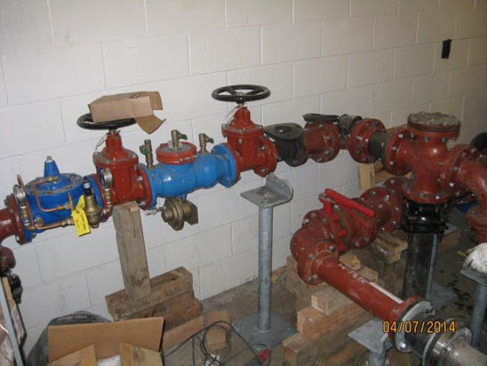Pipes and valves in a utility room, with red and blue components, supported by stands, and some cardboard and wires around.