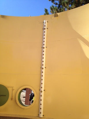 A curved yellow wall with a vertical white pipe and circular window.
